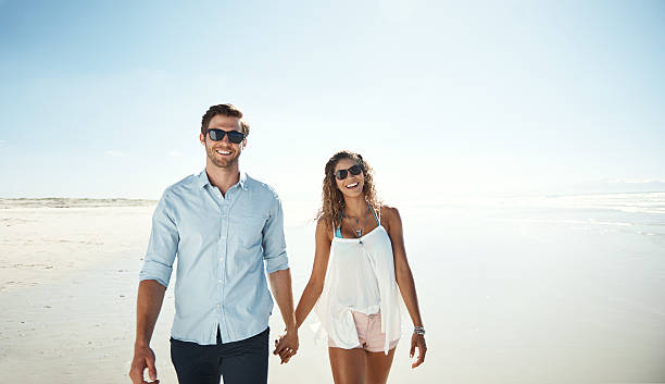 Shot of an affectionate young couple walking hand in hand on the beach